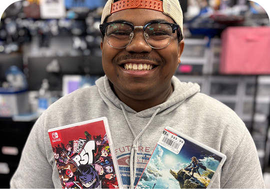 Smiling customer in a game store holding two Nintendo Switch game cases.